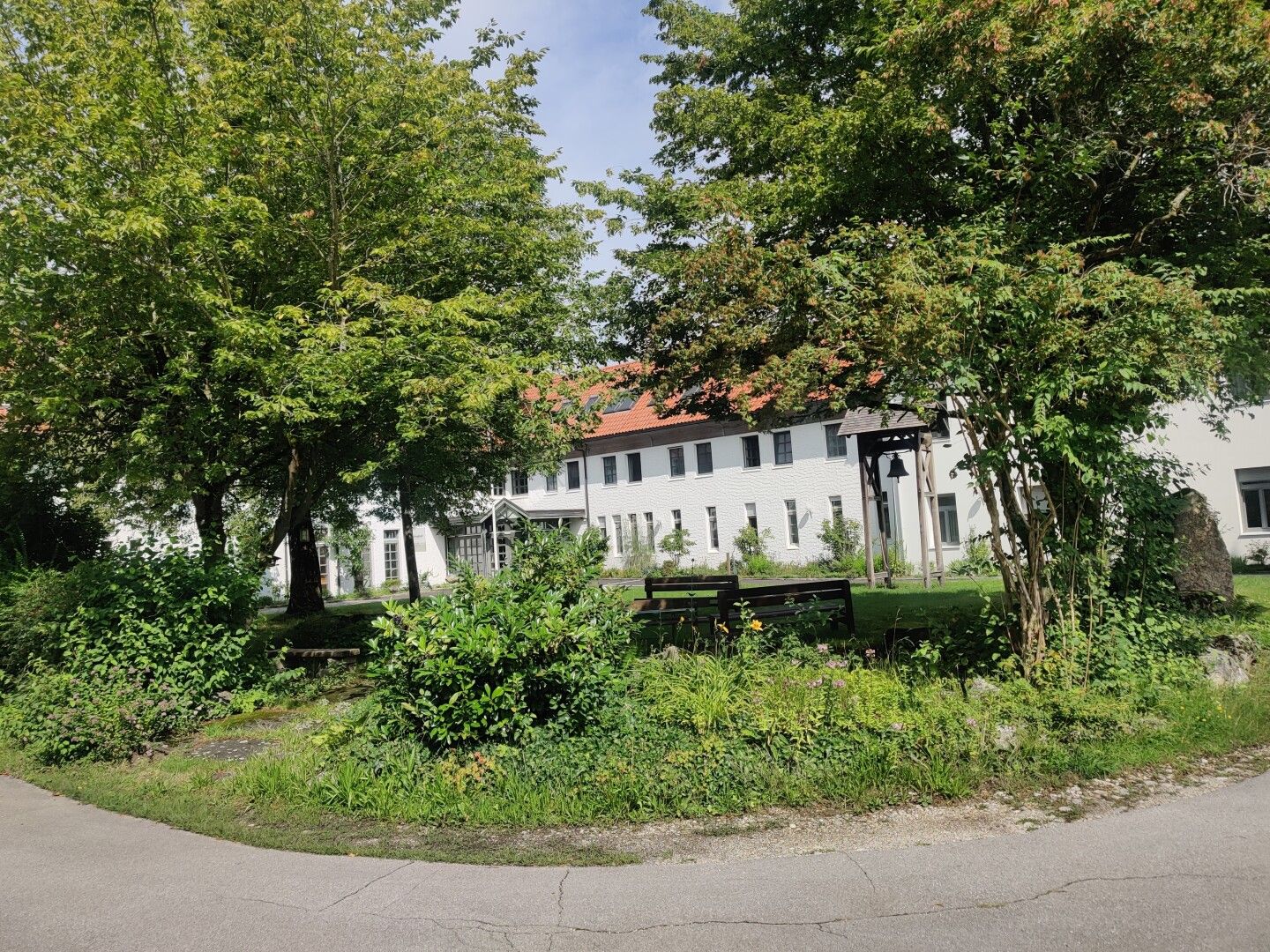 Bāume und Natur. Ganz hinten ist ein langes Gebäude, der Greisinghof.