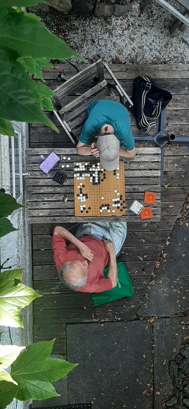 Foto von oben: zwei Personen beim Go Spielen. ich mit Kappe und grünem Shirt und Martin, älterer Herr mit rotem T Shirt.