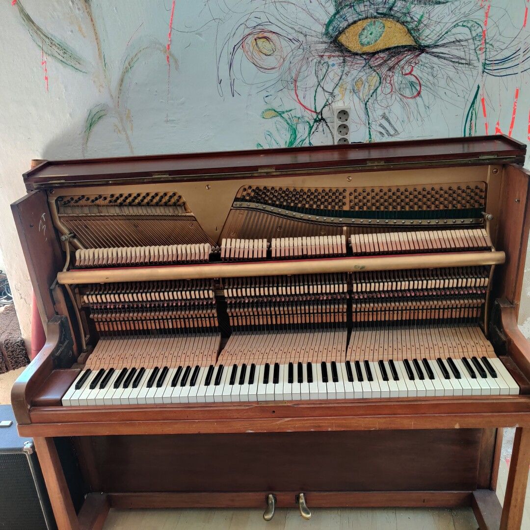 Ein offenes Klavier und darüber auf der Wand ist ein Kunstwerk: Zwei gelbe Augen.